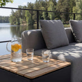 sackit Cobana loungesofa med grå puter og teakbord med oppbevaring ved en innsjø i nordisk utemiljø