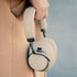 Beige Touch 400 over ear hodetelefoner fra sackit med polstrede øreklokker og hodebøyle holdes mot en beige jakke i mykt naturlig lys