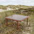 Mollis Coffee Table i chestnut med pulverlakkert aluminiumsramme og røykfarget herdet glass, utendørs bruk.