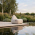 Lys beige loungestol fra sackit på en terrasse ved hagedam omgitt av frodig nordisk natur og speilbilder i vannet