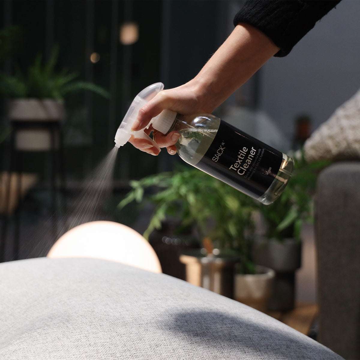 sackit Textile Cleaner sprayes på en lys tekstilsofa for å fjerne flekker og holde møblene rene