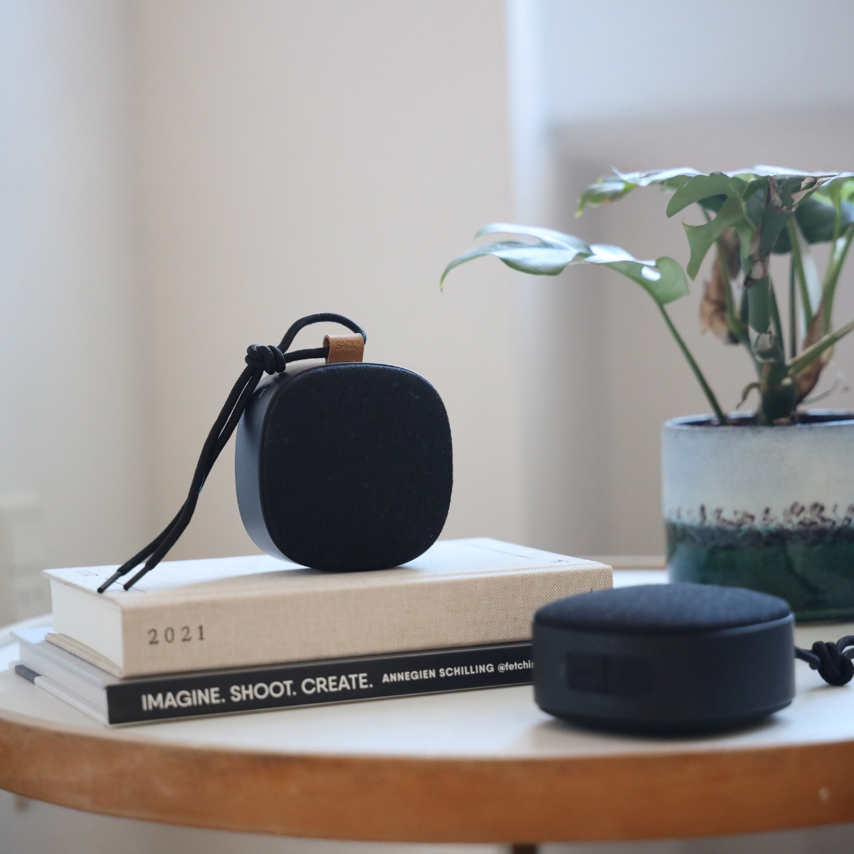 To svarte trådløse høyttalere fra sackit på et rundt trebord med bøker og en grønn plante i bakgrunnen dansk design for hjemmet