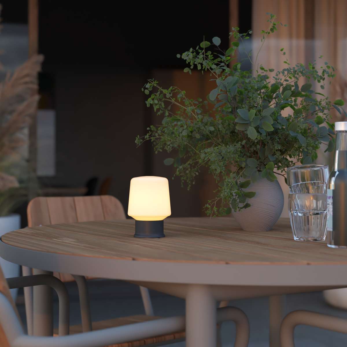 Lysende trådløs bordlampe fra sackit på et rundt trebord i en lun spisestue med grønne planter og glass i bakgrunnen