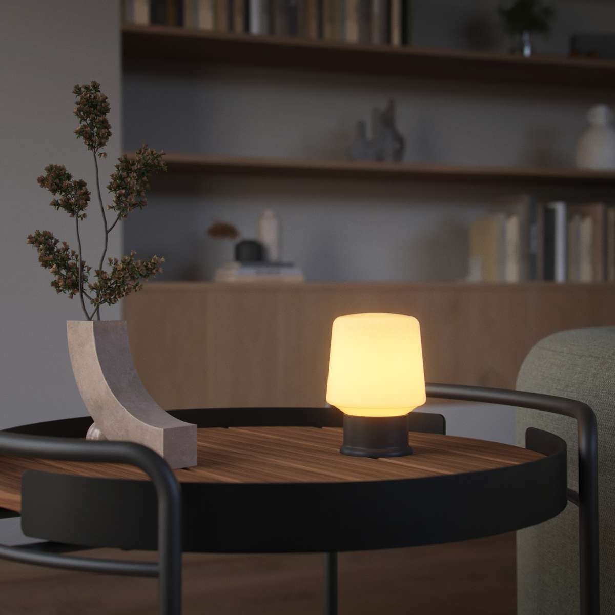 Trådløs bordlampe fra sackit med varmt lys på et rundt trebord i en stilfull nordisk stue med hyller og dekorative detaljer
