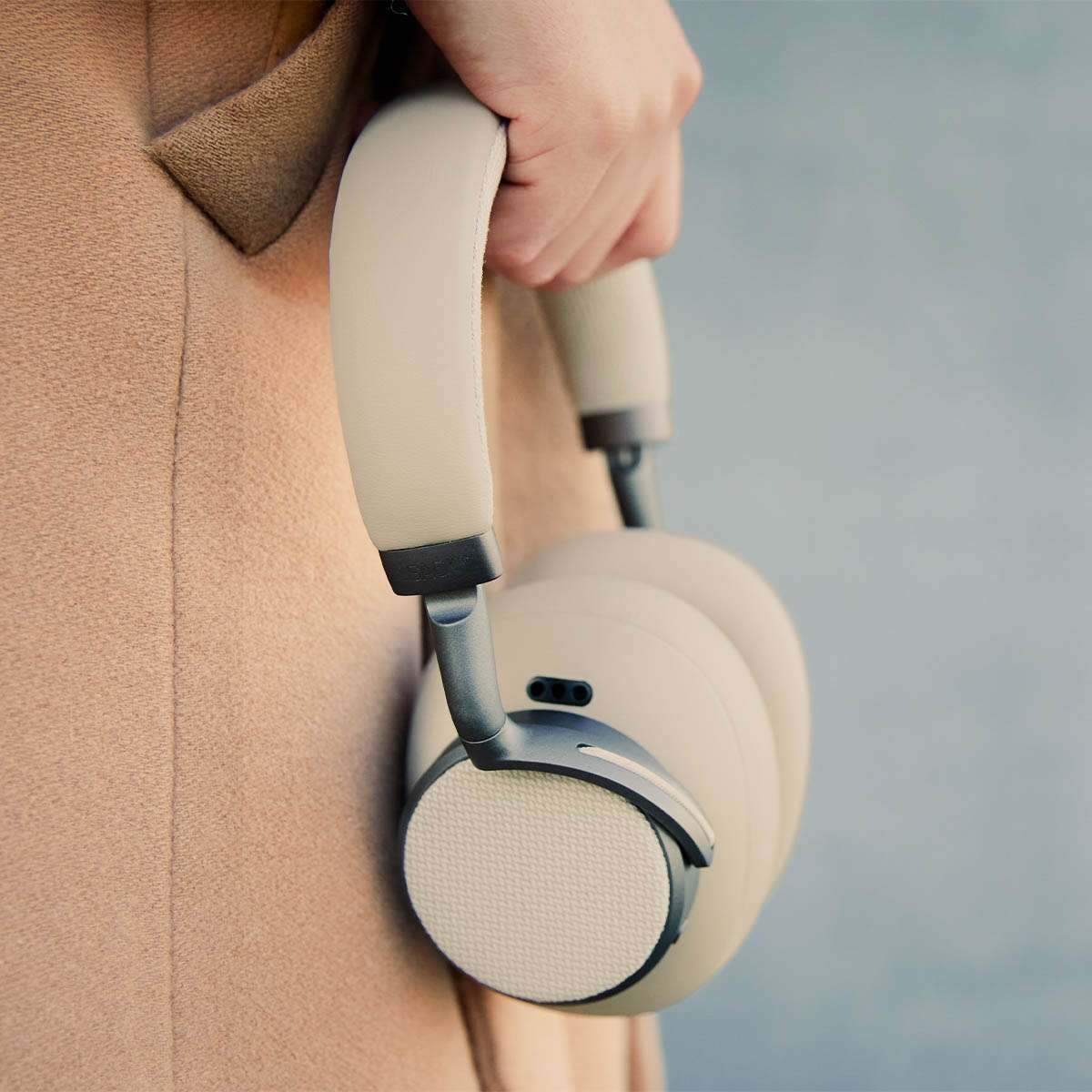 sackit Touch 410 trådløse over ear hodetelefoner i beige med polstrede øreputer og aktiv støydemping holdes i hånden