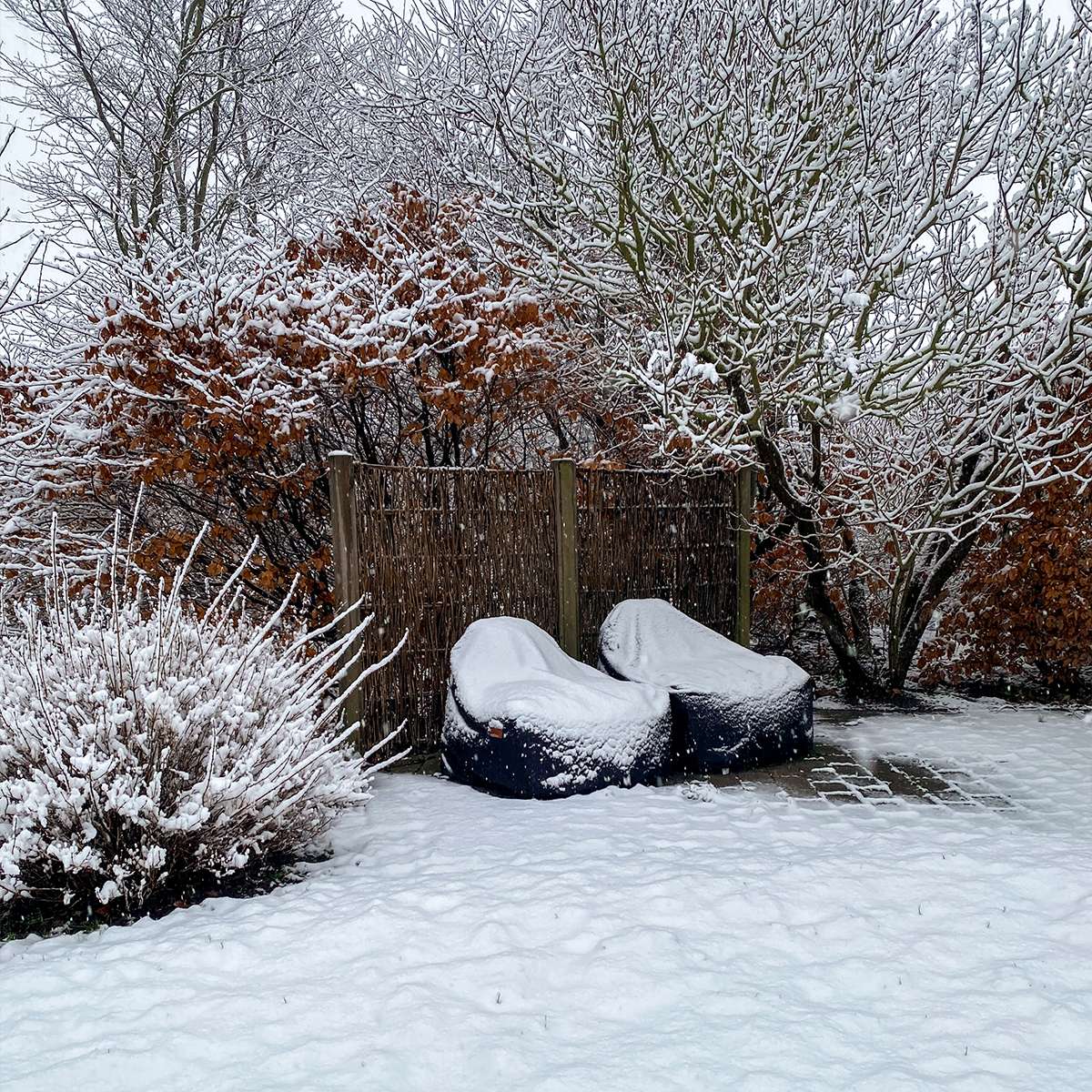 Vannavvisende vintertrekk beskytter to utendørs loungestoler mot snø og vintervær i en snødekt hage.
