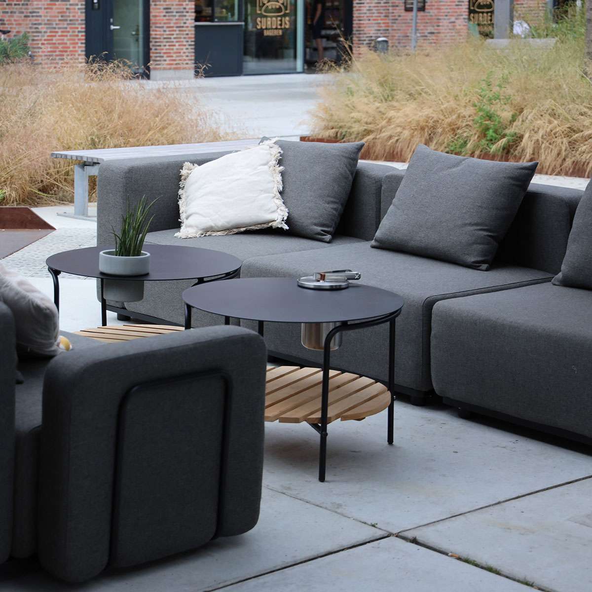Grå modulsofa med hjørnedel og puter på terrasse med lave svarte bord og naturlige omgivelser fra sackit Norway