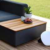 Sort modulsofa fra sackit med teakbord med oppbevaring plante og frukt på terrasse i nordisk hagemiljø
