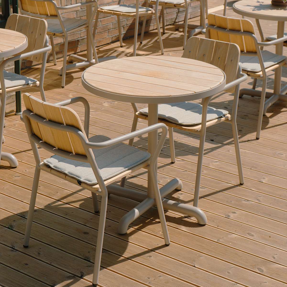 Rundt kafébord i teak og pulverlakkert aluminium på en solrik terrasse med moderne stoler fra sackit for nordisk uteliv