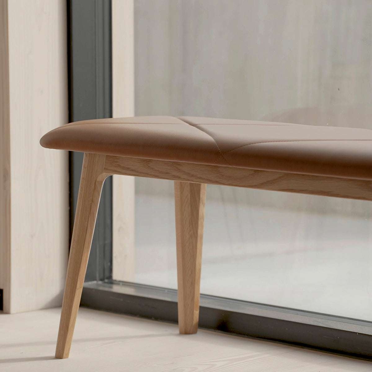 Nordic Bench in oak with Terra Black leather seat and smooth wooden frame in a simple setting.