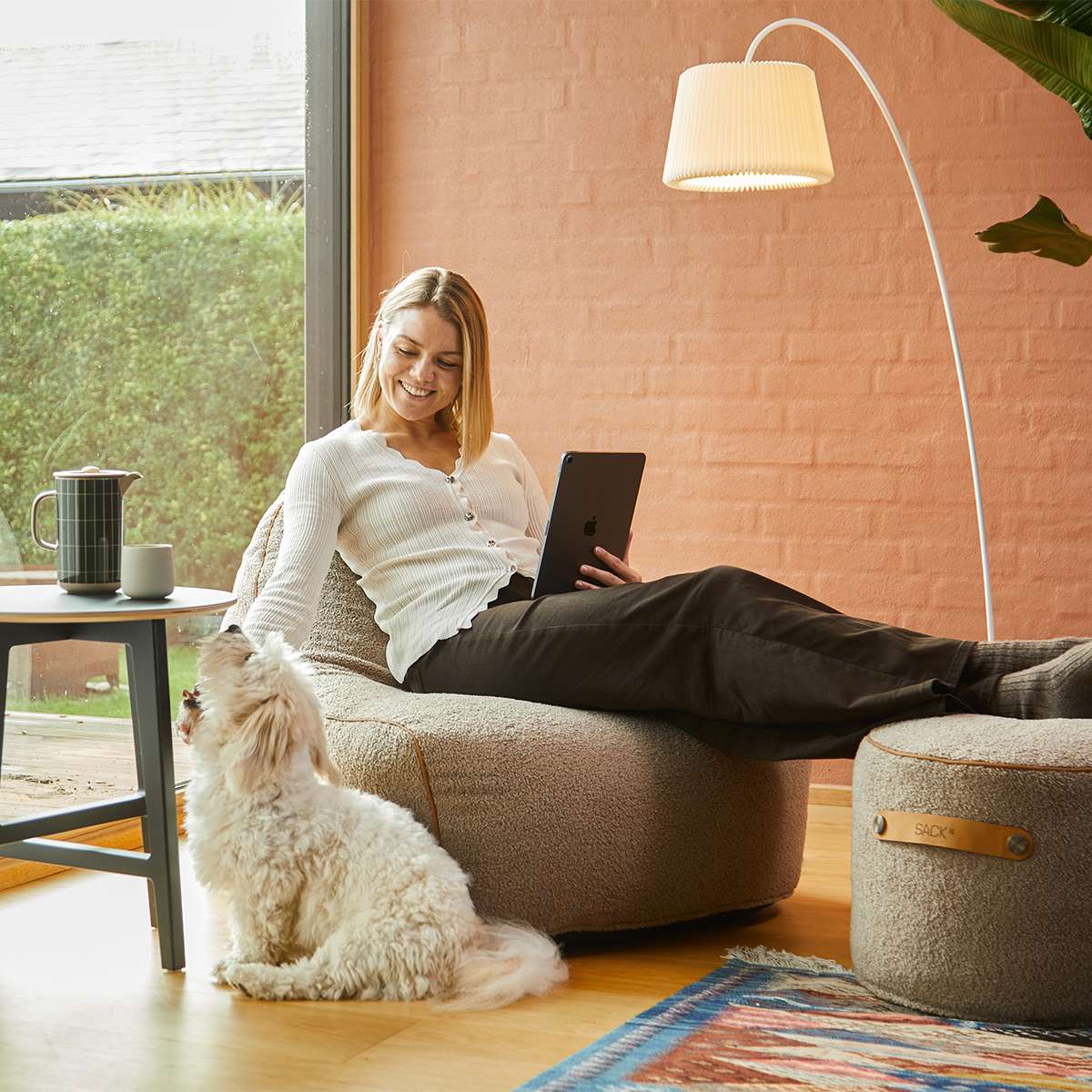 sackit loungestol innendørs med kvinne som bruker nettbrett og hund i en varm stue med matchende puff teppe og gulvlampe