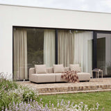 Beige Cobana loungesofa med tre sitteplasser på en solrik terrasse omgitt av grønne planter og blomsterkledd hagepergola