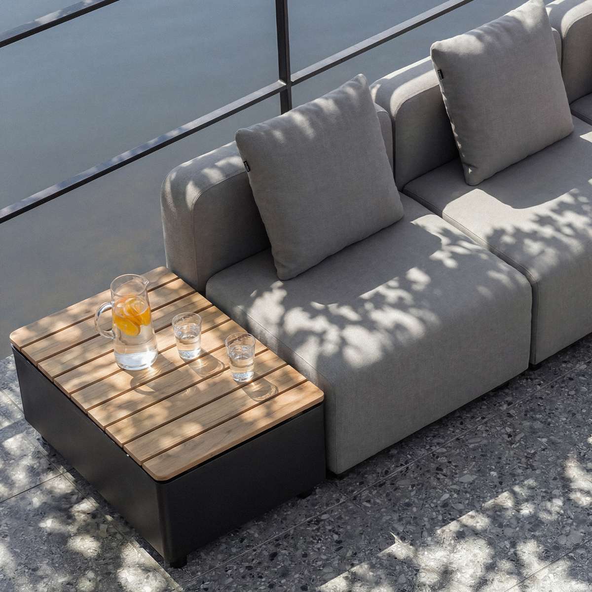 Grå modulbasert Cobana loungesofa fra sackit på terrasse med puter og sidebord i tre og sort metall designet for nordisk utendørsbruk