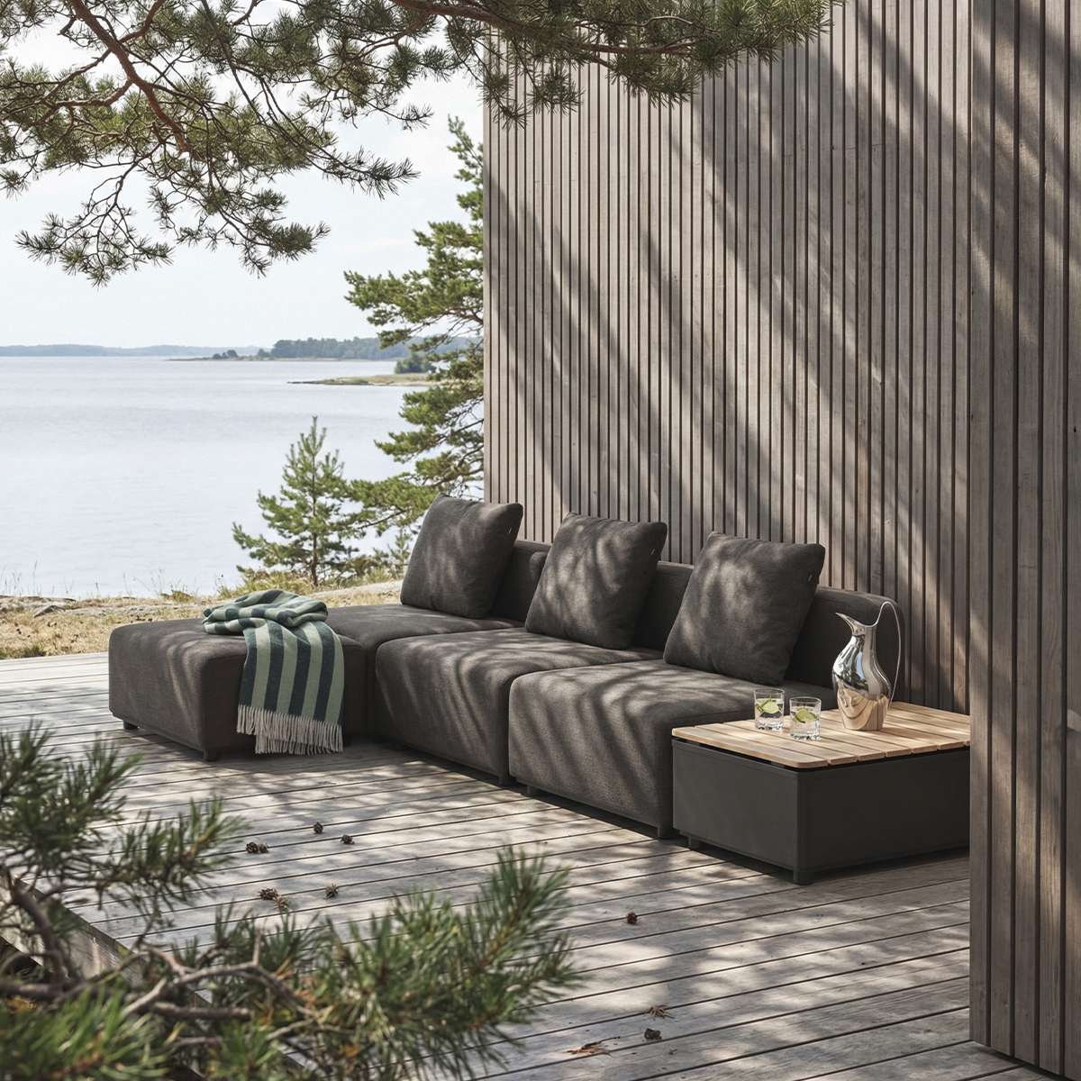 Modulbasert Cobana loungesofa fra sackit på treterrasse ved sjøen med mørke puter puff og sidebord i et nordisk utemiljø