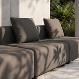 Mørk grå modulbasert utesofa fra sackit med myke ryggputer på en solrik terrasse foran en betongvegg og grønne planter