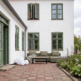 Olivegrønn tre seters loungesofa på en sjarmerende gårdsplass med hage og blomster, omgitt av hvite husvegger og grønne vinduskarmer