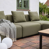 Olivengrønn modulbasert utesofa fra sackit med myke puter og pledd på en lun terrasse i en grønn hage