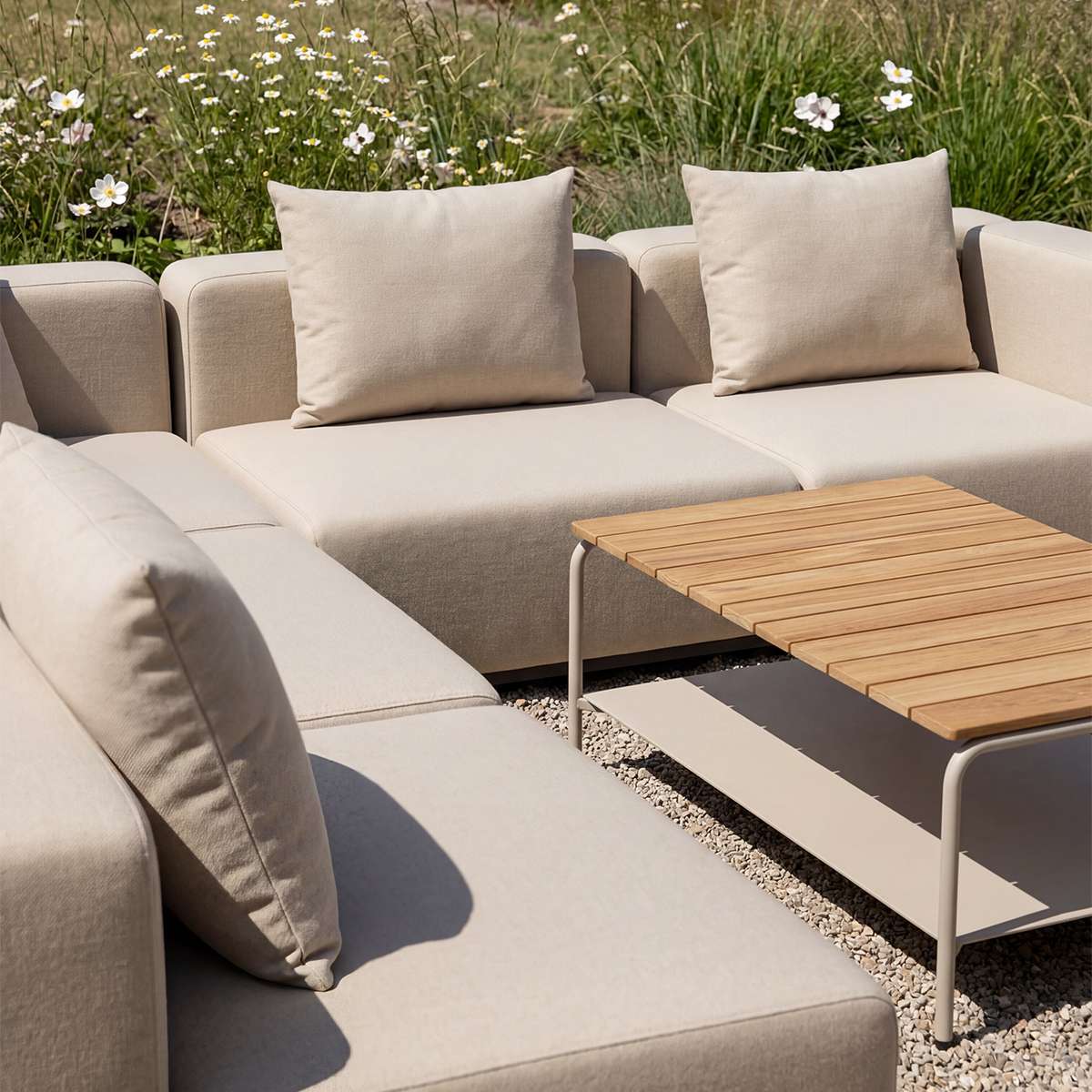 Beige modulær utesofa med myke puter og hjørneoppsett rundt et lavt utebord i tre på en solrik terrasse omgitt av blomsterenger