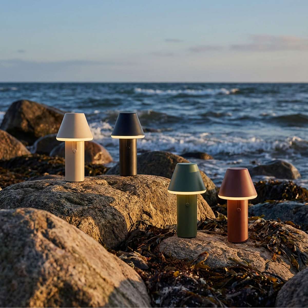 Fire trådløse Cone bordlamper fra sackit plassert på svaberg ved havet med mykt lys og fargerike skjermer for utendørs bruk