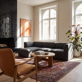 Mørk grå Fjord sofa med venstrevendt sjeselong i lys nordisk stue med mønstret teppe trebord peis og store vinduer fra sackit