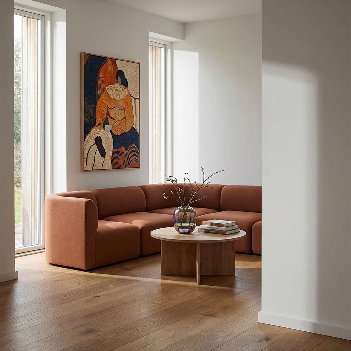 Brun Fjord hjørnesofa fra sackit i en lys nordisk stue med kunst på veggen rundt sofabord og grønne grener
