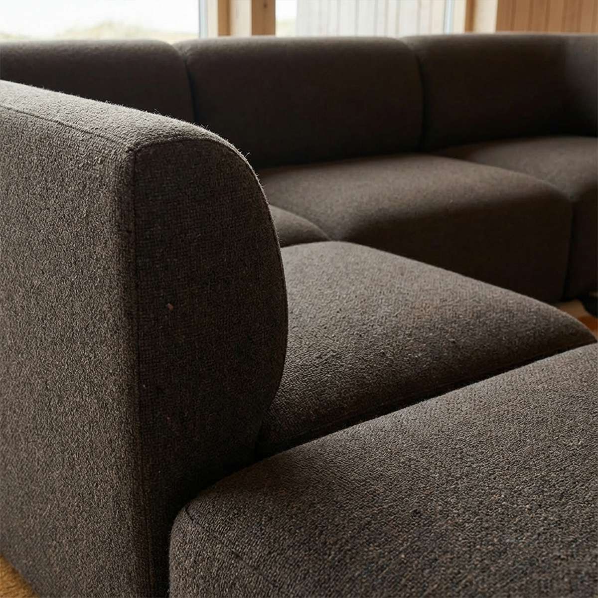 Nærbilde av mørk brun Fjord hjørnesofa fra sackit med myke avrundede former og tekstiltrekk i en lun nordisk stue