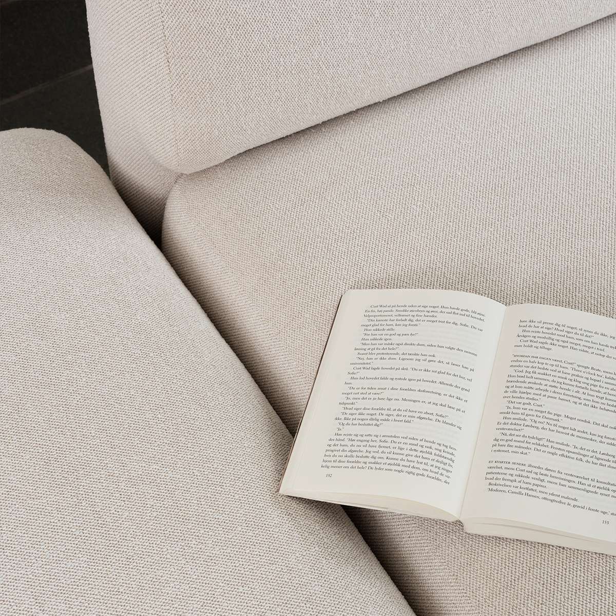 Nærbilde av en lys tekstilsofa med myke avrundede former og en åpen bok på setet fra sackit i skandinavisk design