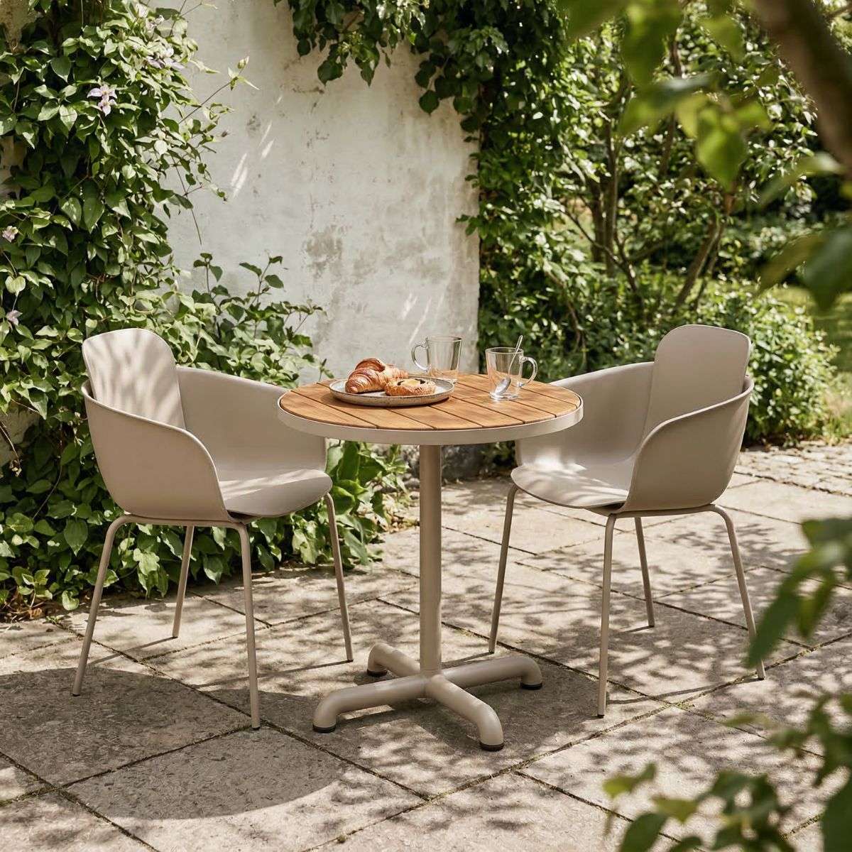 Rundt utebord i tre med to taupe hagestoler fra sackit på en solrik terrasse omgitt av frodig grønt og klatreplanter