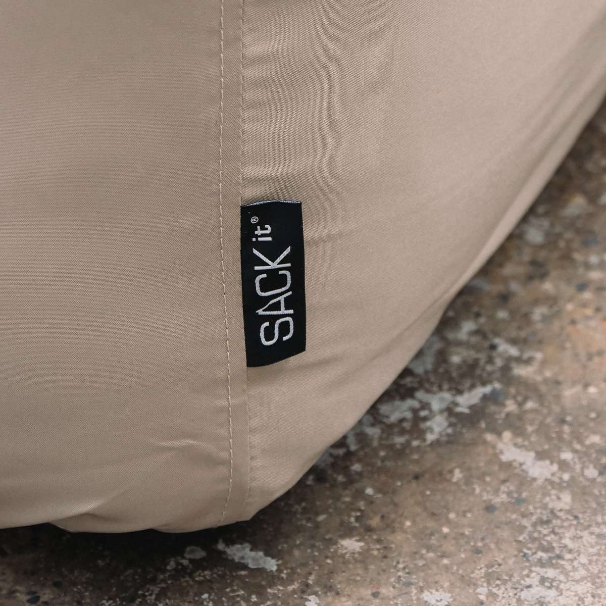 Detalj av beige trekk til Soft Sofa pouf med synlig søm og sackit merke, designet for å beskytte utemøbelet mot vær og vind