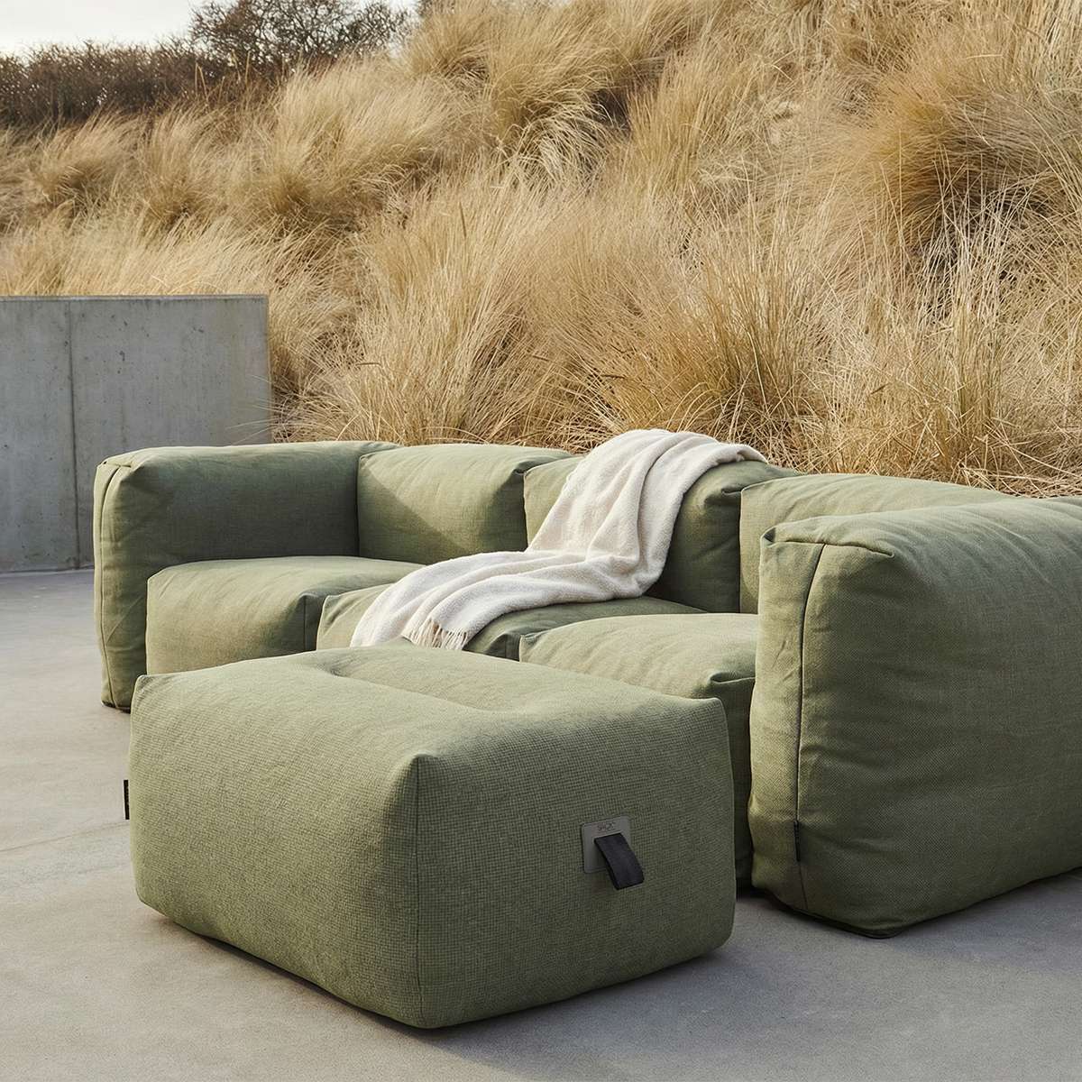 Grønn Soft Sofa utendørs puff fra sackit i en lun loungeløsning med sofa og pledd på terrasse omgitt av høyt strandgress