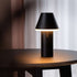 Sort trådløs bordlampe med konisk skjerm og mykt varmt lys på et mørkt bord. sackit Cone for innendørs og utendørs bruk