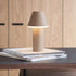 Trådløs bordlampe fra sackit i pulverlakkert aluminium med varmt lys på en bunke bøker ved et trebord innendørs