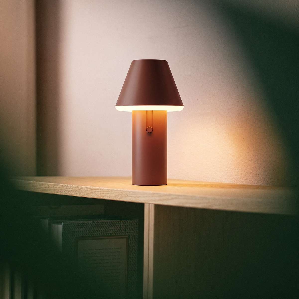 Brun trådløs bordlampe fra sackit med varmt lys på en trehylle i et stilrent interiør