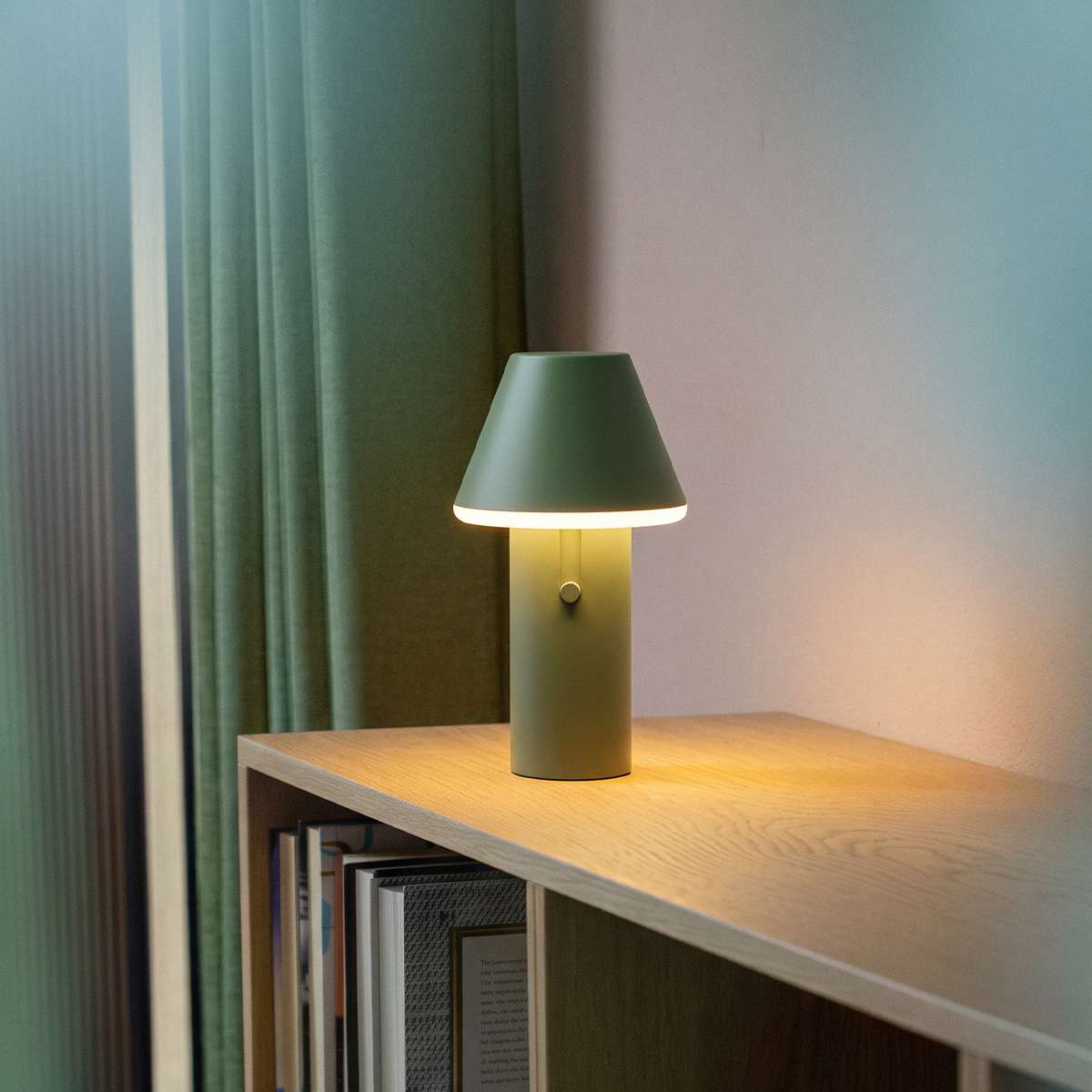 Grønn trådløs bordlampe i pulverlakkert aluminium fra sackit med mykt lys på en trehylle i et nordisk interiør