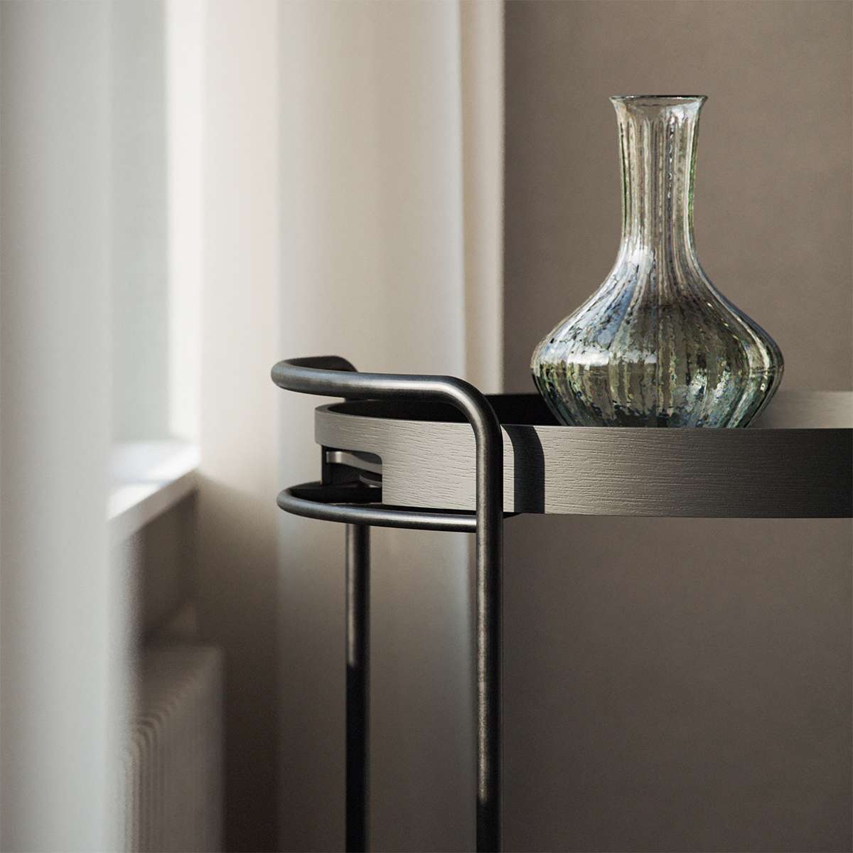 Svart sidebord med slank metallramme og dekorativ glassvase ved et lyst vindu fra sackit