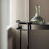 Svart sidebord med slank metallramme og dekorativ glassvase ved et lyst vindu fra sackit