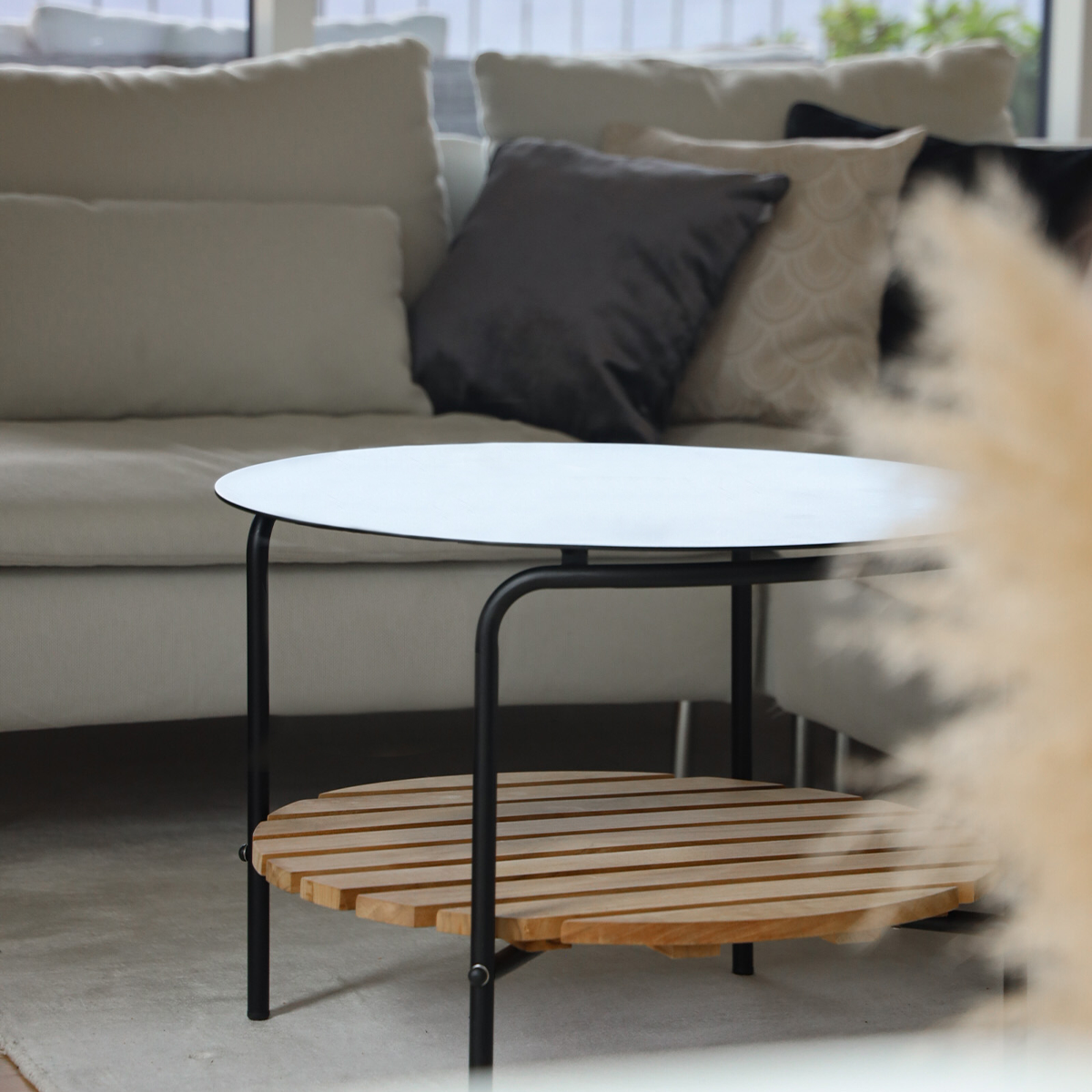 Rundt utendørs sofabord i sort pulverlakkert aluminium med teak bordplate og rene linjer.