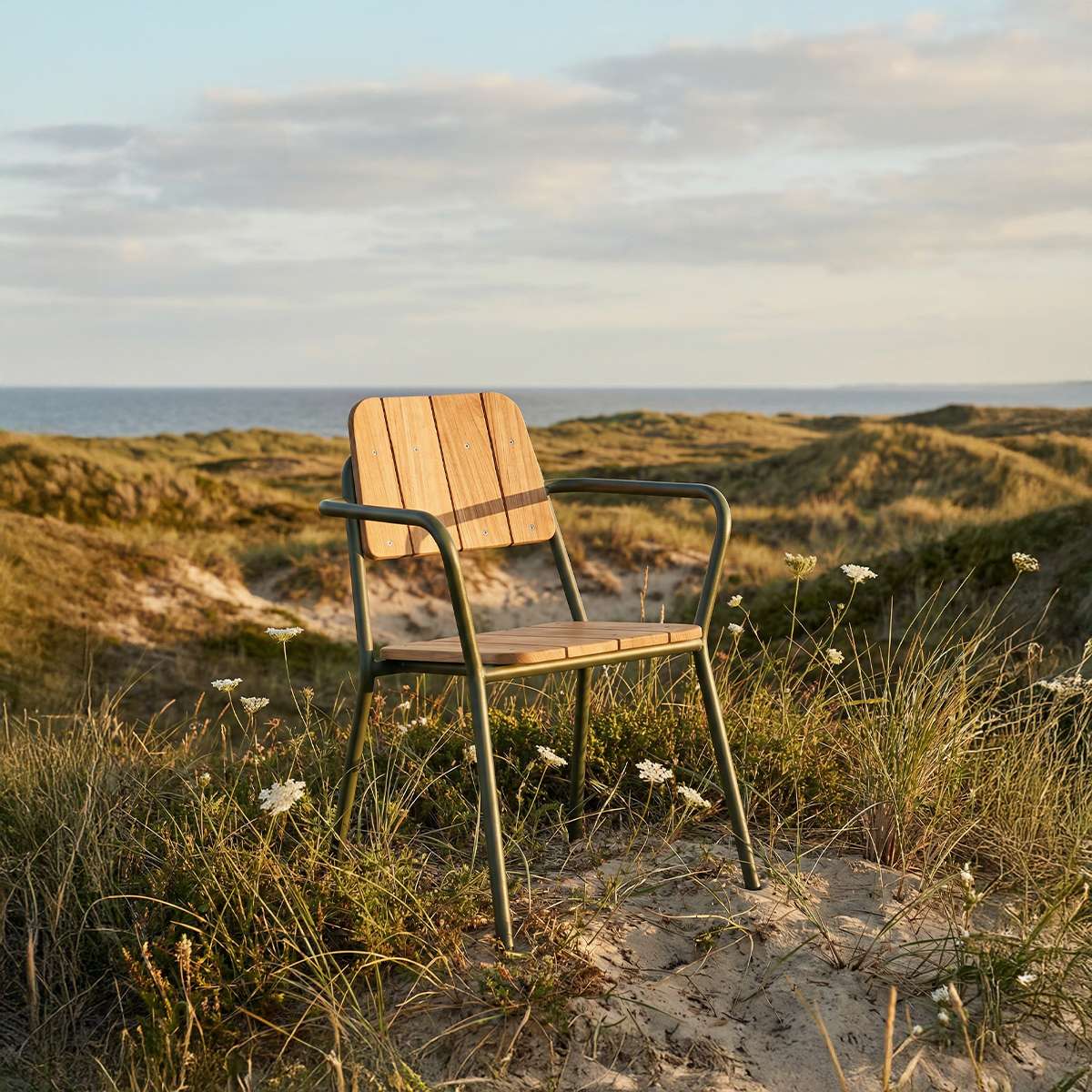 sackit Kirra hagestol i aluminium og teak plassert mellom marehalm og sanddyner med havet i bakgrunnen ved nordisk kystlandskap