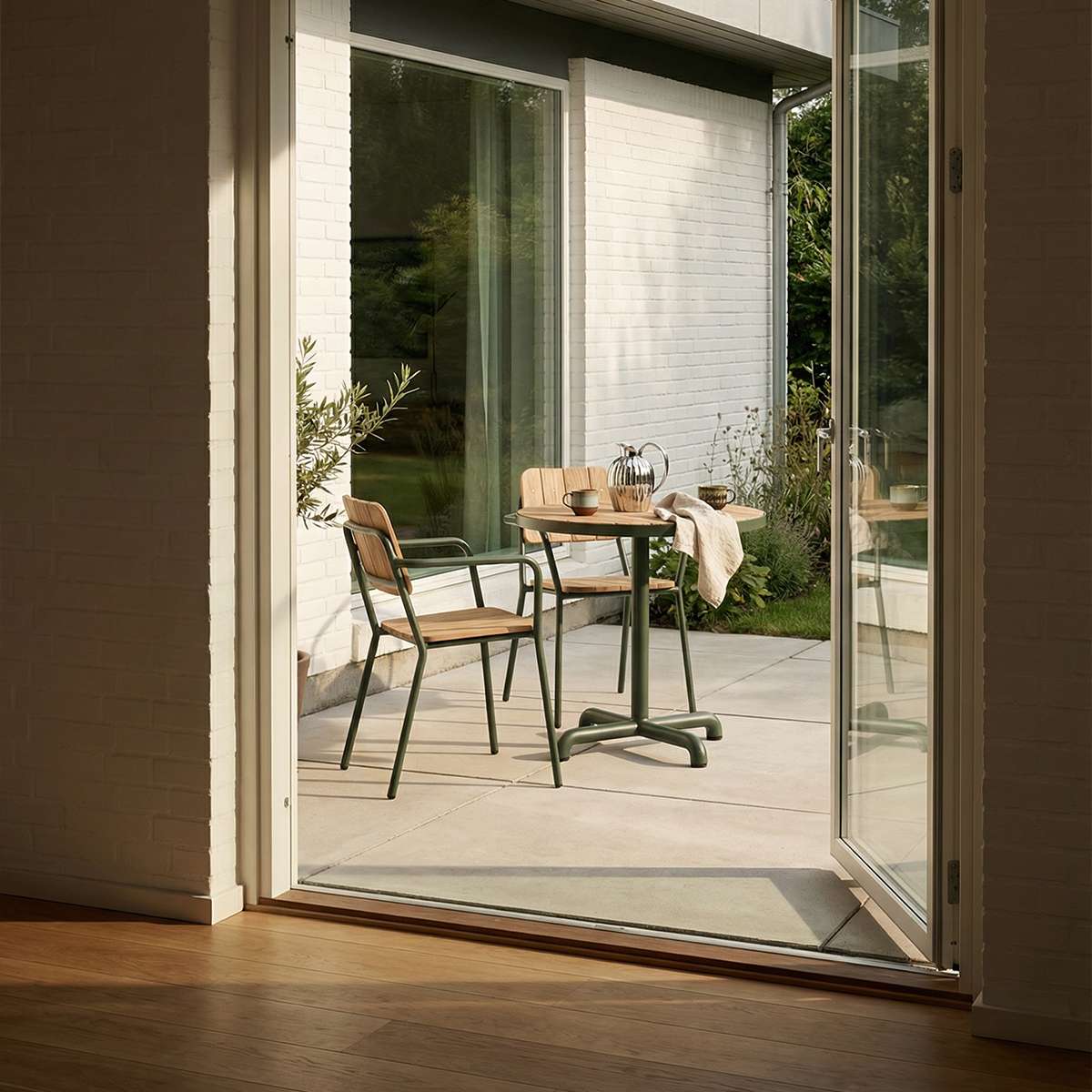 To elegante Kirra hagestoler i pulverlakkert aluminium og teak rundt et lite utebord på en solrik terrasse ved åpne glassdører