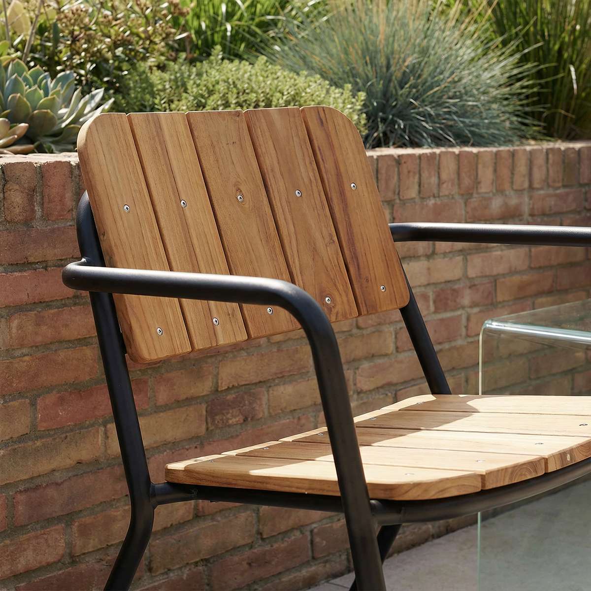 Kirra Patio Lounge Chair i svart pulverlakkert aluminium og ubehandlet teak, lav og avslappet sittestilling.