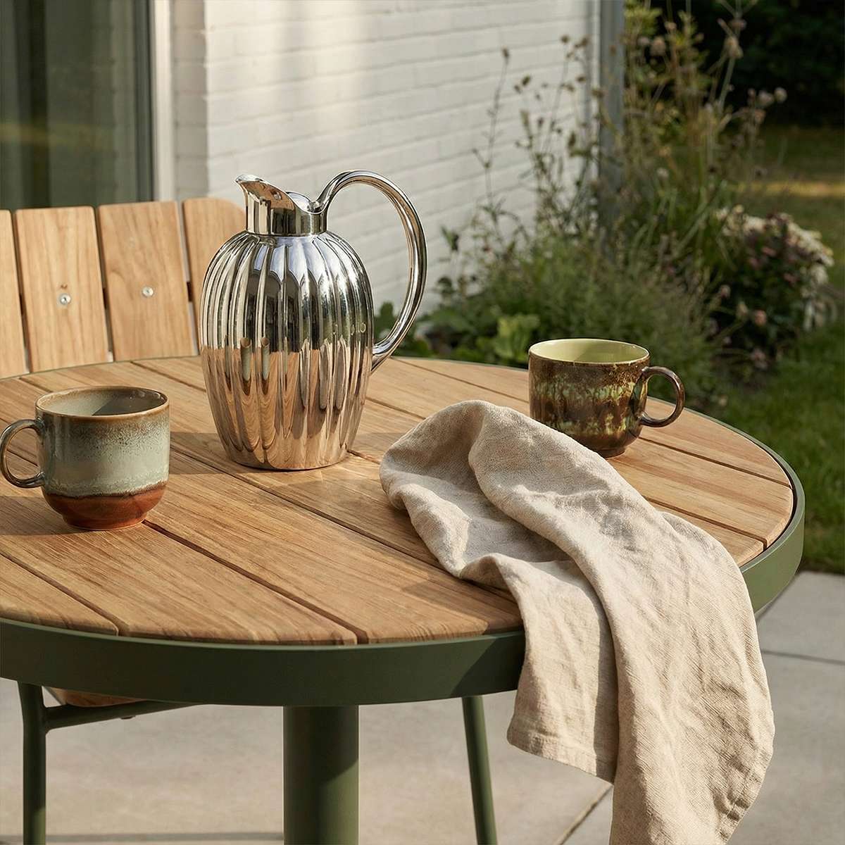 Kirra Café Table utendørs bord i pulverlakkert aluminium og ubehandlet teak, rund form, naturfarger.