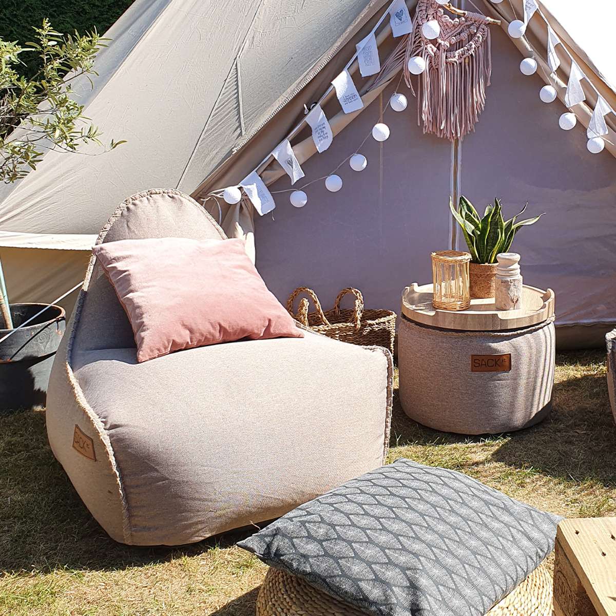 Lys loungestol i canvas med rosa pute og gråmønstret puff i en hyggelig teltcamping fra sackit