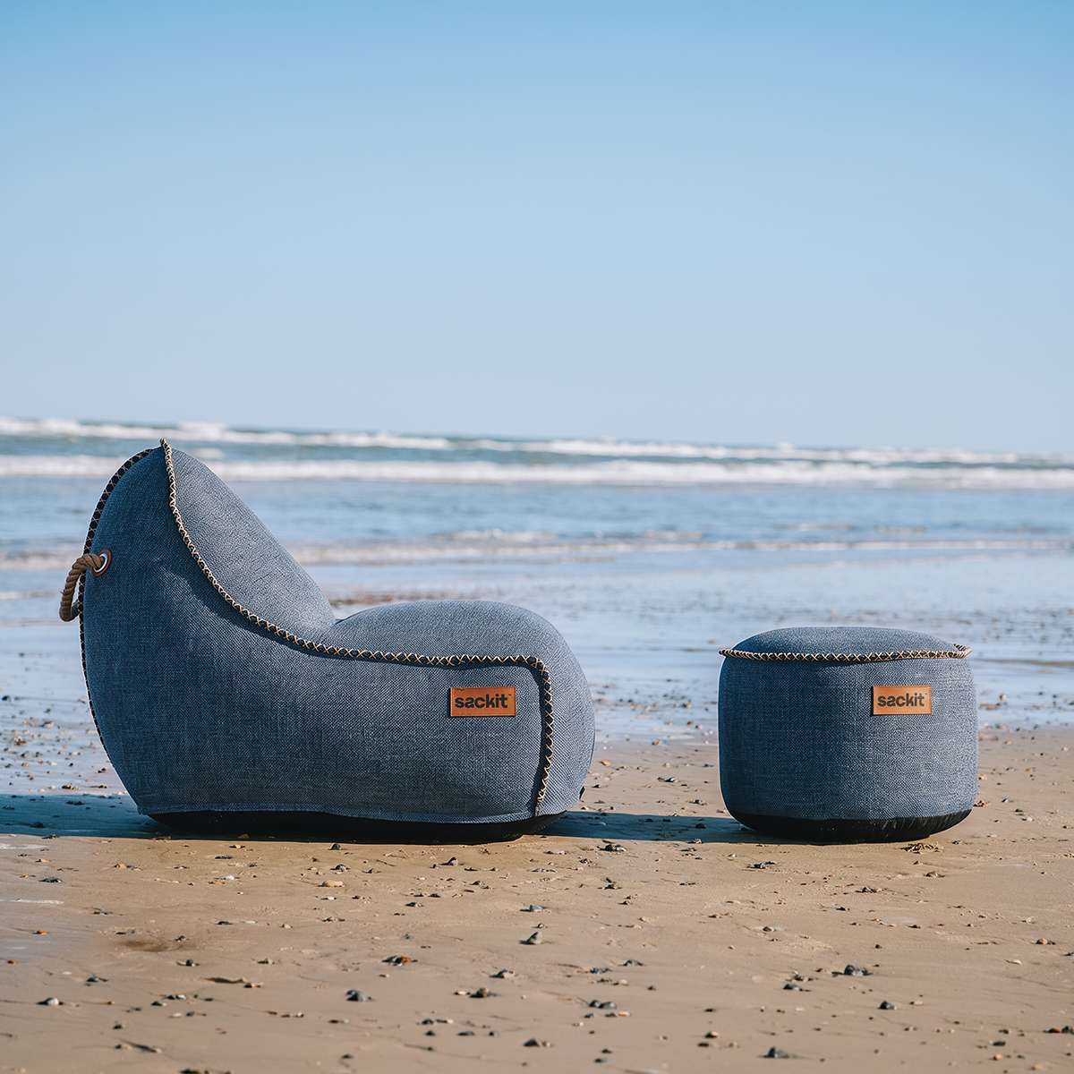 sackit Cobana loungestol og puff i værbestandig stoff står på en sandstrand med havet i bakgrunnen