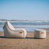 sackit Cobana loungestol og puff i lyst tekstil på en sandstrand med havet i bakgrunnen, designet for avslapping utendørs