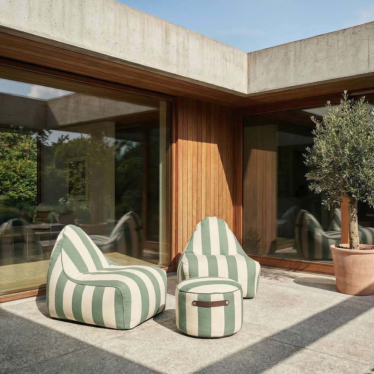 sackit utendørs loungestoler i grønt og hvitt stripemønster på en solrik terrasse ved et moderne hus med store vinduer og oliventre