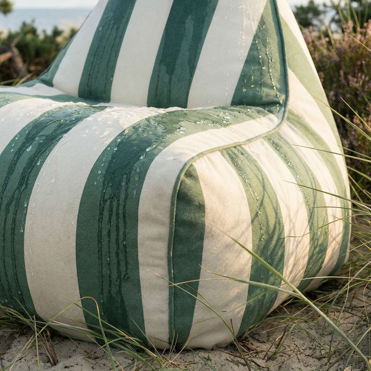 sackit utendørsstol i grønt og kremfarget stripemønster med vannperler på stoffet omgitt av gress og sand i nordisk utemiljø