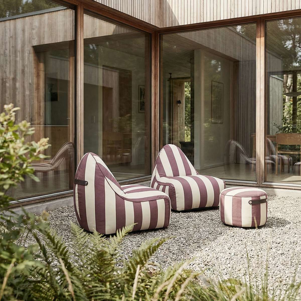 Stripete sackit loungestoler og puff i burgunder og krem på en gruslagt terrasse foran et moderne trehus med store glassflater