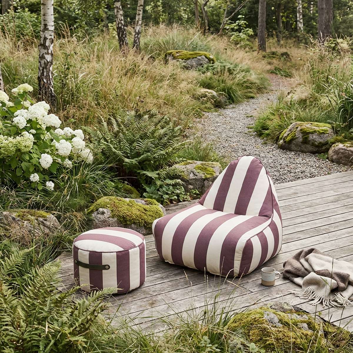 sackit stripete utendørs loungestol med puff på en treterrasse, omgitt av frodig hage, mosegrodde steiner, pledd og en kopp