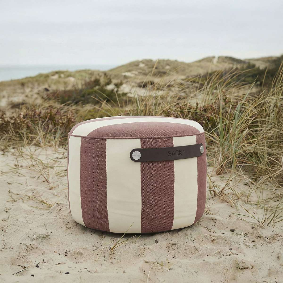 Stripete sackit utendørs puff i beige og burgunder med bærestropp på sanddynene ved stranden for nordisk utebruk
